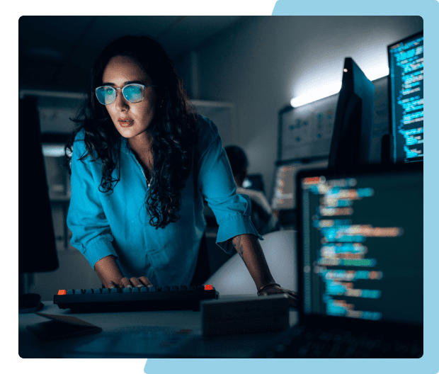 Woman coding on computer in dimly lit room.